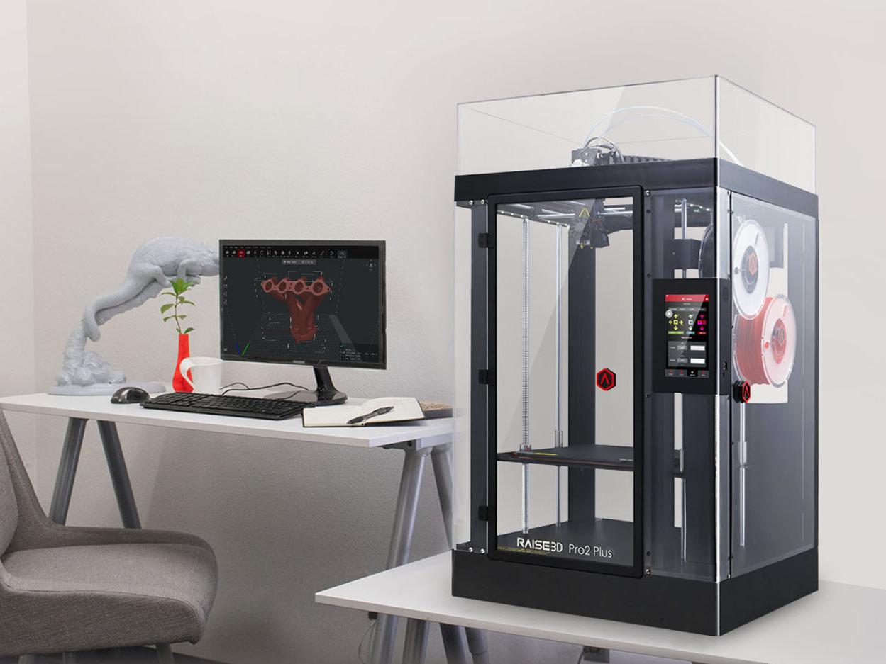Raise3d Pro2 Plus steht auf einem Tisch neben einem Schreibtisch mit Computer