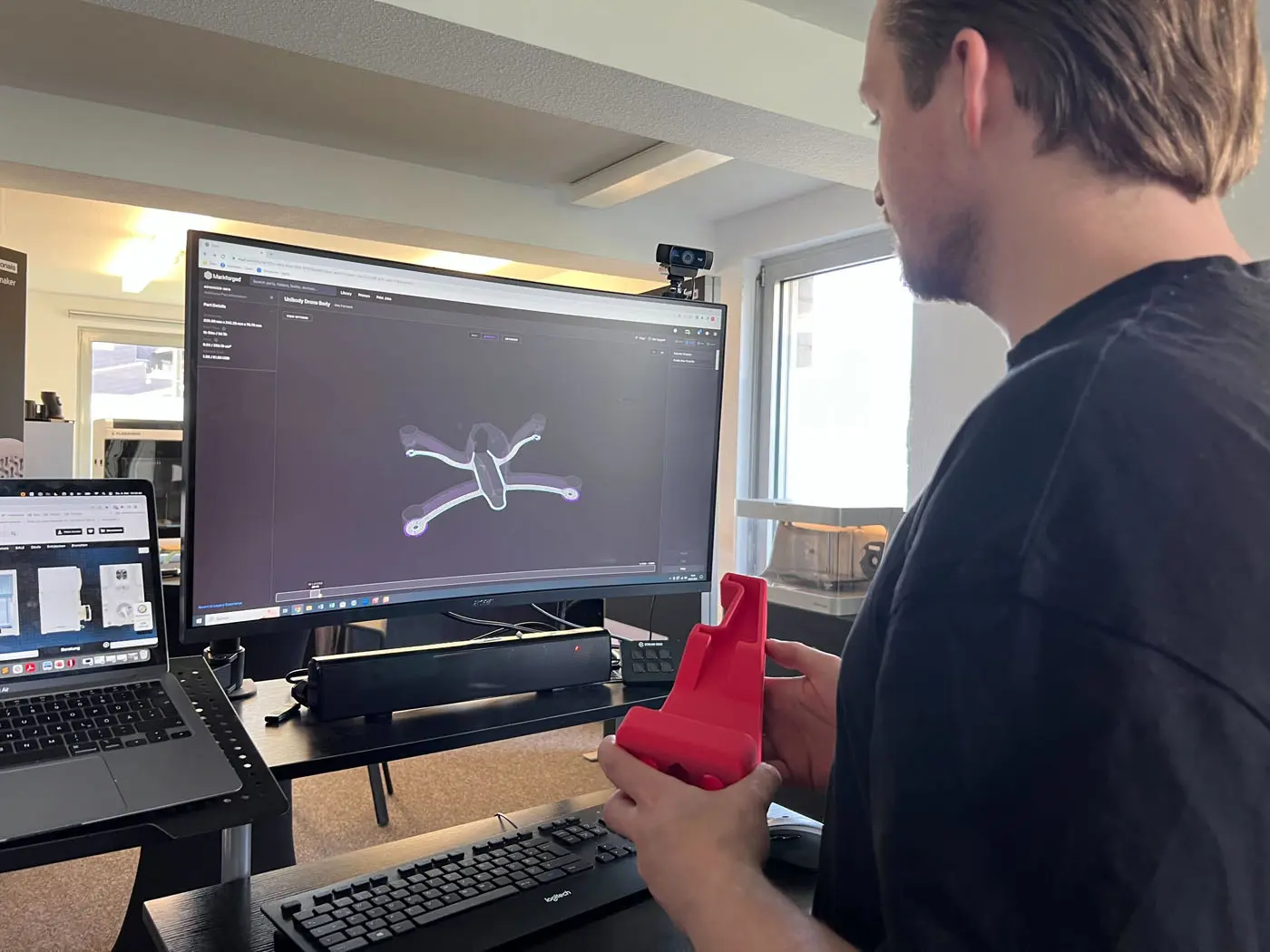 Jemand steht vor einem Computer und schaut auf den Monitor mit einem 3D gedruckten Stück in seiner Hand