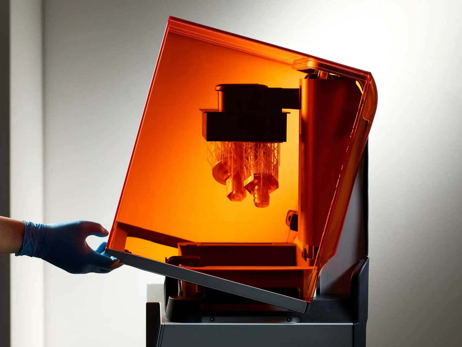 Formlabs Form 4 fertiger Druck. Eine Hand mit Gummihandschuh öffnet den 3D Drucker SLA
